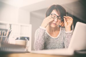 Tired woman rubbing her eyes in front of her computer