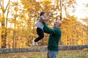 Grandad playing with grandson and lifting him into the air on an autumnal day