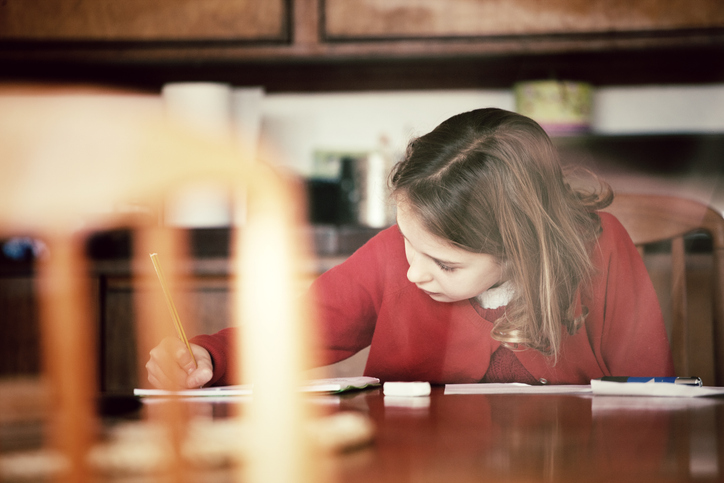 A young girl doing her homework, sitting at the kitchen table.