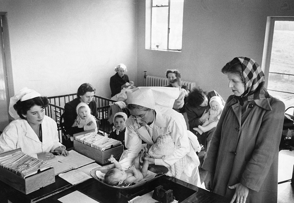 A nurse weighs the infant daughter of one of the Lawrence Weston Health Centre's patrons, Bristol, circa 1950.